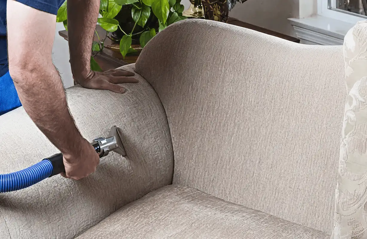 Professional upholstery cleaner deep-cleaning a fabric sofa with a handheld extraction tool and hose, Charleston, SC.